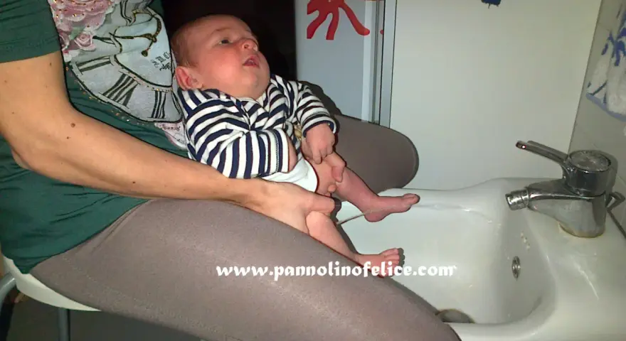 Un bimbo fa pipì in giro mentre è seduto sul lavandino, con un adesivo di polpo sul muro.