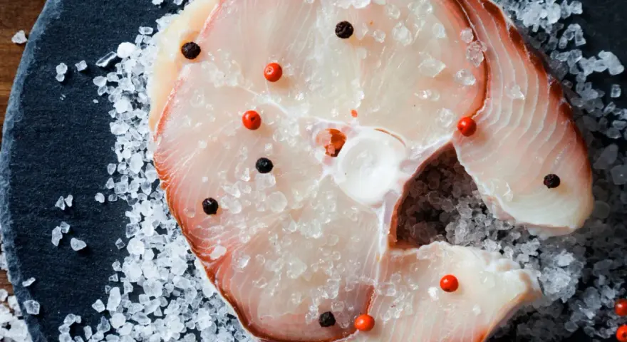 Raw swordfish steak with salt and peppercorns on a dark slate.