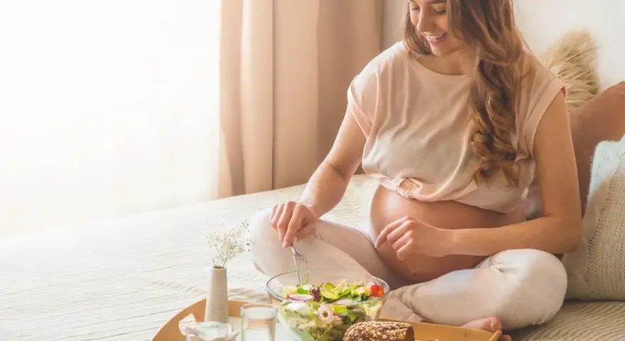 Donna incinta sorride mangiando un'insalata fresca. Il burro in gravidanza è un alimento importante per la crescita del feto.