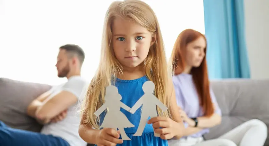 Bambina con sagome di carta di una coppia, mentre i genitori separati sono sullo sfondo.