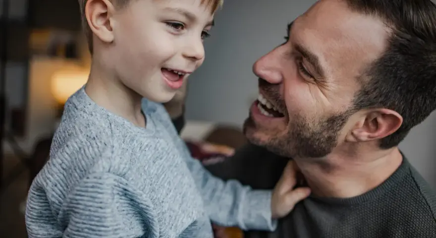 Un padre e suo figlio ridono guardandosi negli occhi. Il bambino, con un maglione grigio, sembra chiedere "perché mio figlio non mi chiama mamma?".