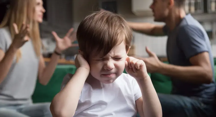 Bambino con le mani sulle orecchie, mentre i genitori litigano. Una scena che mostra una crisi di coppia con figli.