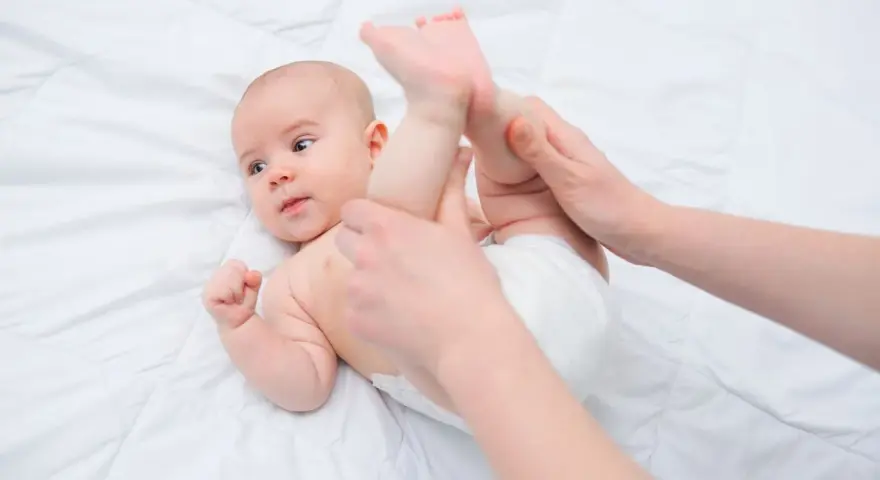 Mani che aiutano un neonato a liberarsi dall'aria nella pancia, con le gambine sollevate delicatamente.