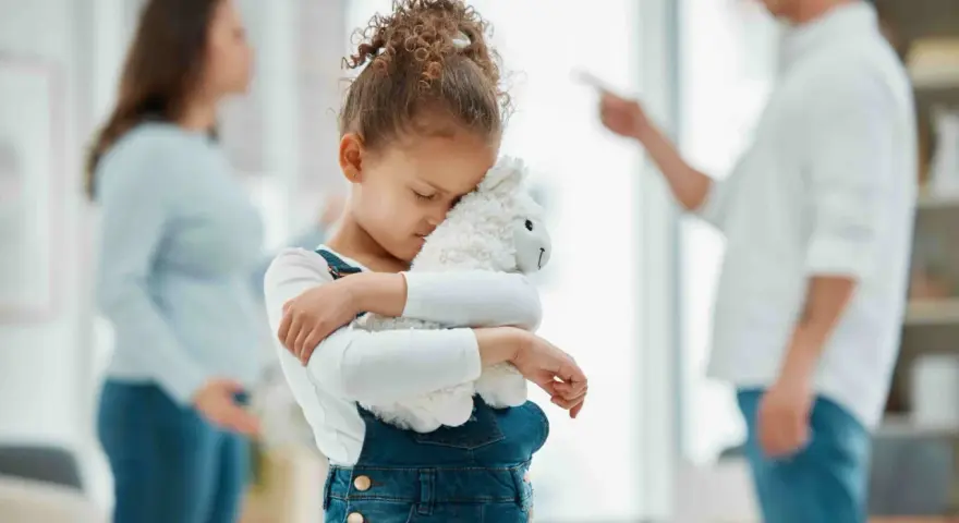 Bambina abbraccia peluche, turbata dalle liti dei genitori separati.