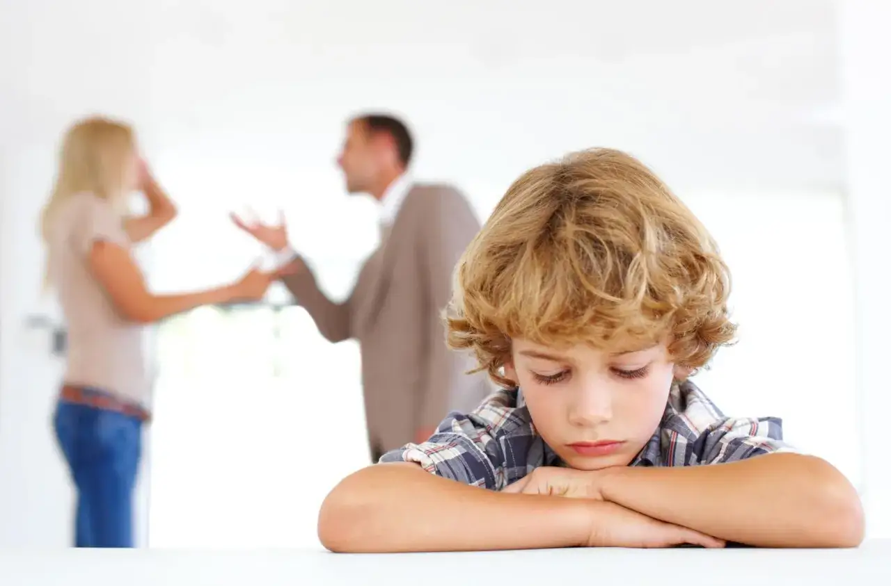 Bambino triste, con genitori che litigano sullo sfondo, simbolo dei traumi dei figli di genitori separati.