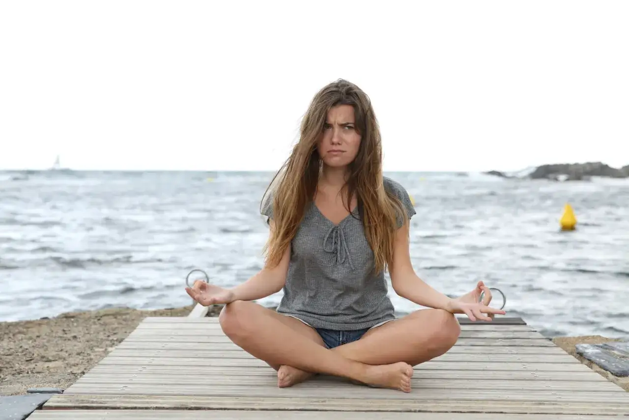Donna in meditazione sulla spiaggia, con espressione corrucciata, forse per capire le cause degli attacchi di rabbia.