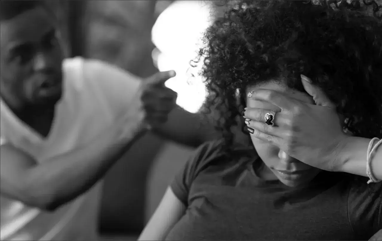 Una donna copre gli occhi, mentre un uomo le punta il dito contro. L'immagine evoca il trauma da violenza psicologica.
