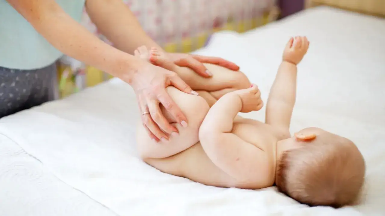 Mani che aiutano il neonato a fare la cacca con movimenti delicati sulle gambine.