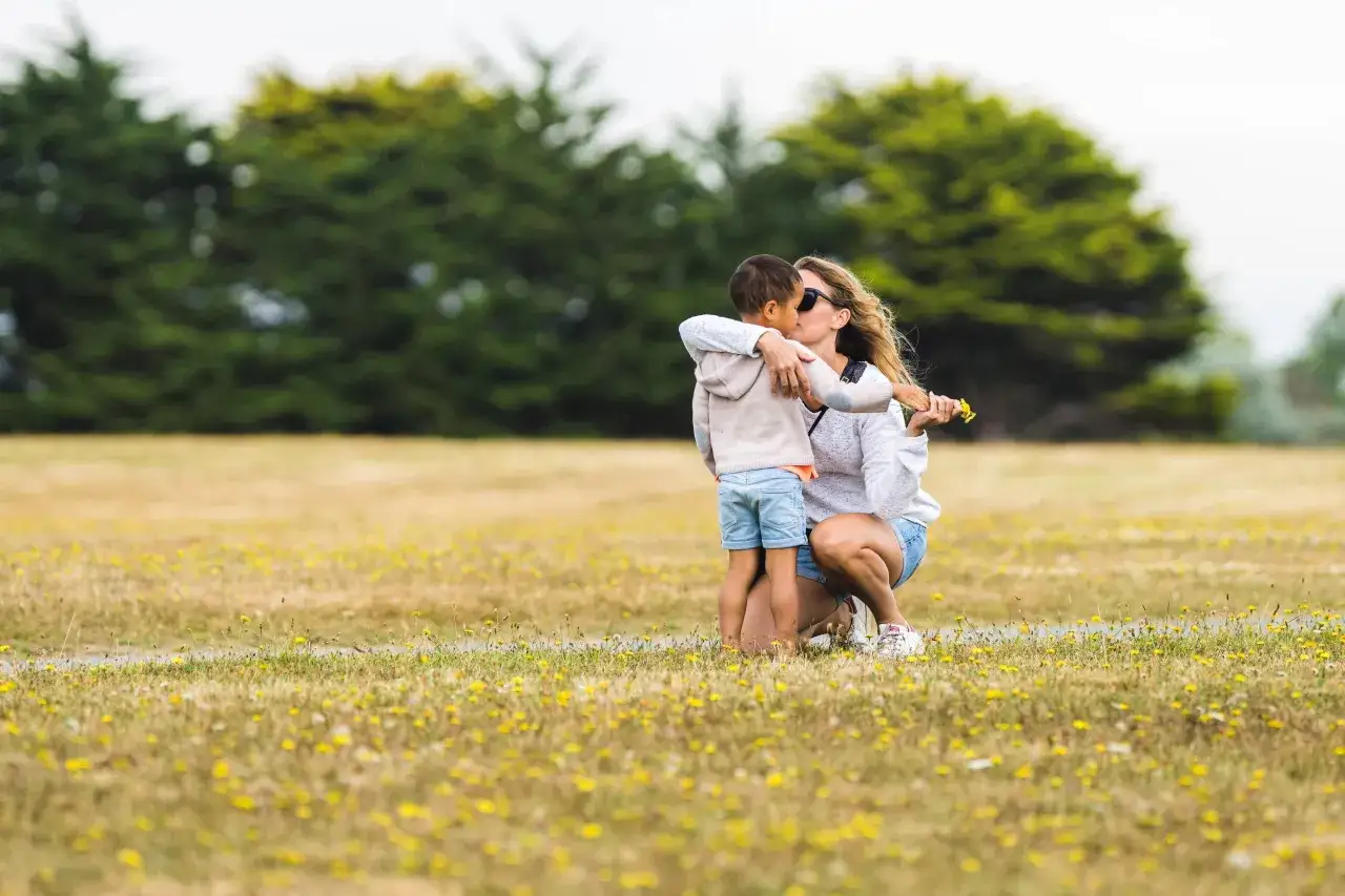 Mamma abbraccia il figlio in un prato fiorito, un momento di tenerezza che insegna come farsi ascoltare dai bambini con amore.
