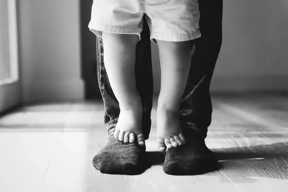 Gambe di un padre e della sua piccola figlia femmina, che si tengono per mano. Un momento di tenerezza tra padre e figlia.