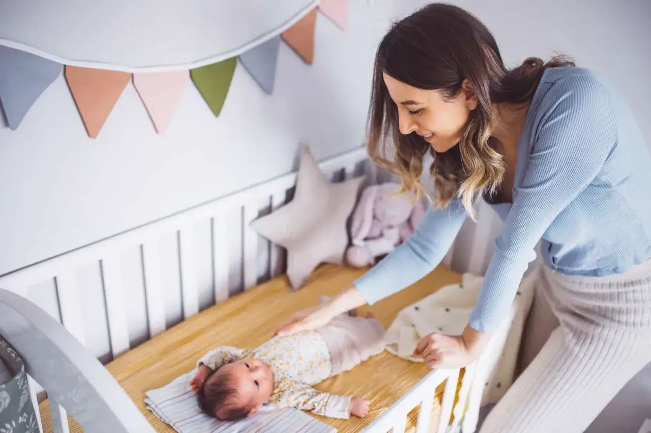 Mamma accarezza il suo neonato nella culla, circondata da decorazioni colorate. Momenti di tenerezza e finestre di veglia piene d'amore.