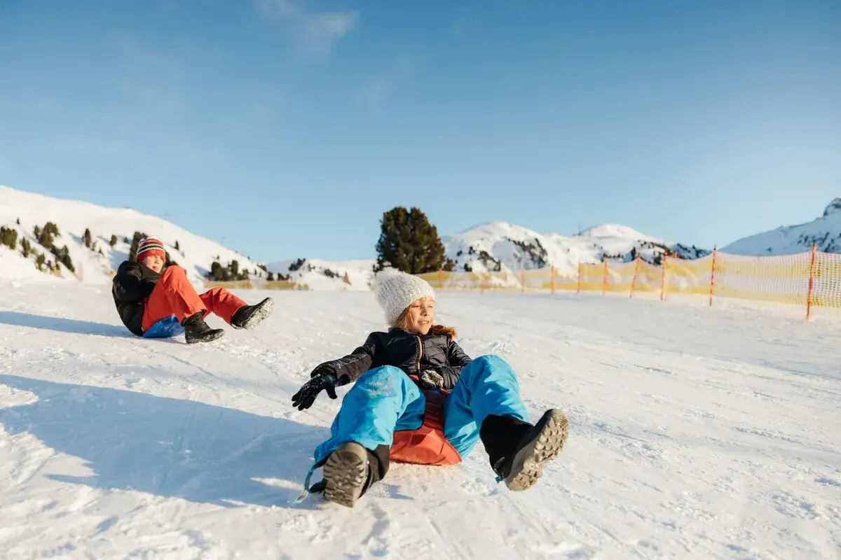 Bambini felici scendono con lo slittino su un pendio innevato, godendosi il divertimento dei neonati in montagna.