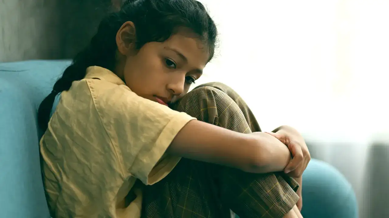 Bambina di 10 anni rannicchiata, con espressione pensierosa, che riflette l'ansia nei bambini di 10 anni.