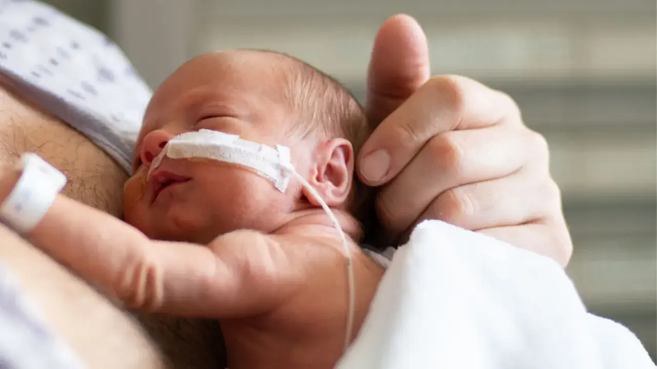Un neonato prematuro, con sondino nasogastrico, è tenuto tra le braccia di un genitore. La montata lattea non arriva, ma l'amore è già presente.