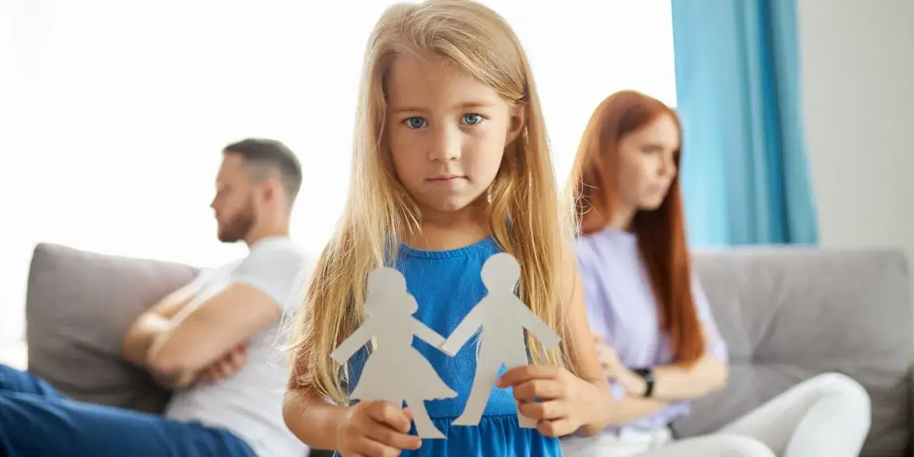 Bambina con sagome di carta di una coppia, mentre i genitori separati sono sullo sfondo.