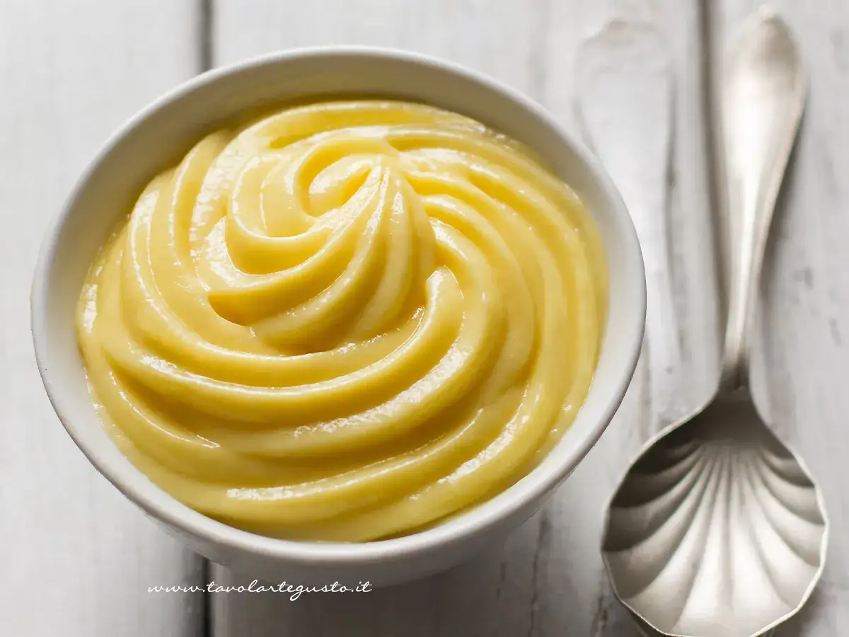 Una ciotola di vellutata crema pasticcera, perfetta per soddisfare le voglie in gravidanza. Accanto, un cucchiaio d'argento.