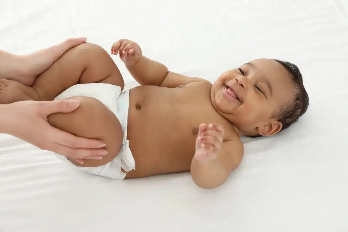 Bambino sorridente su un lettino, con le gambe piegate, in una delle posizioni per stimolare la cacca dei neonati.