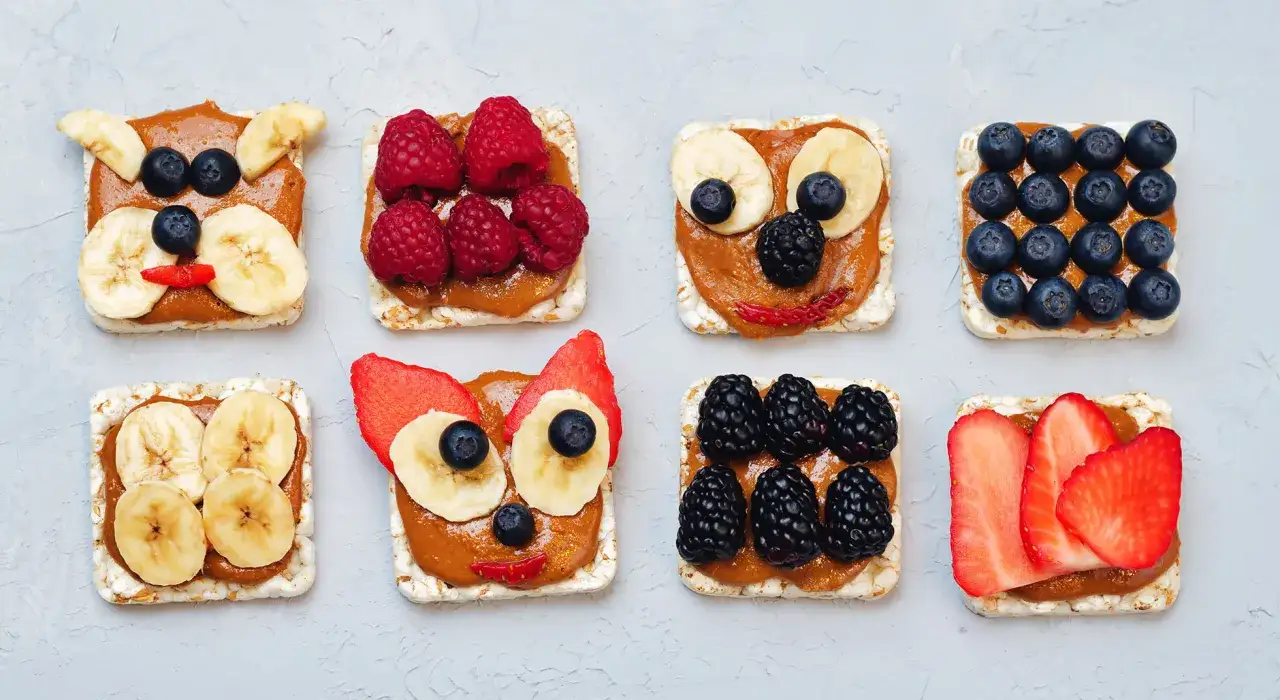 Deliziose merende per bambini: gallette di riso con crema di arachidi e frutta, decorate come faccine di animali.