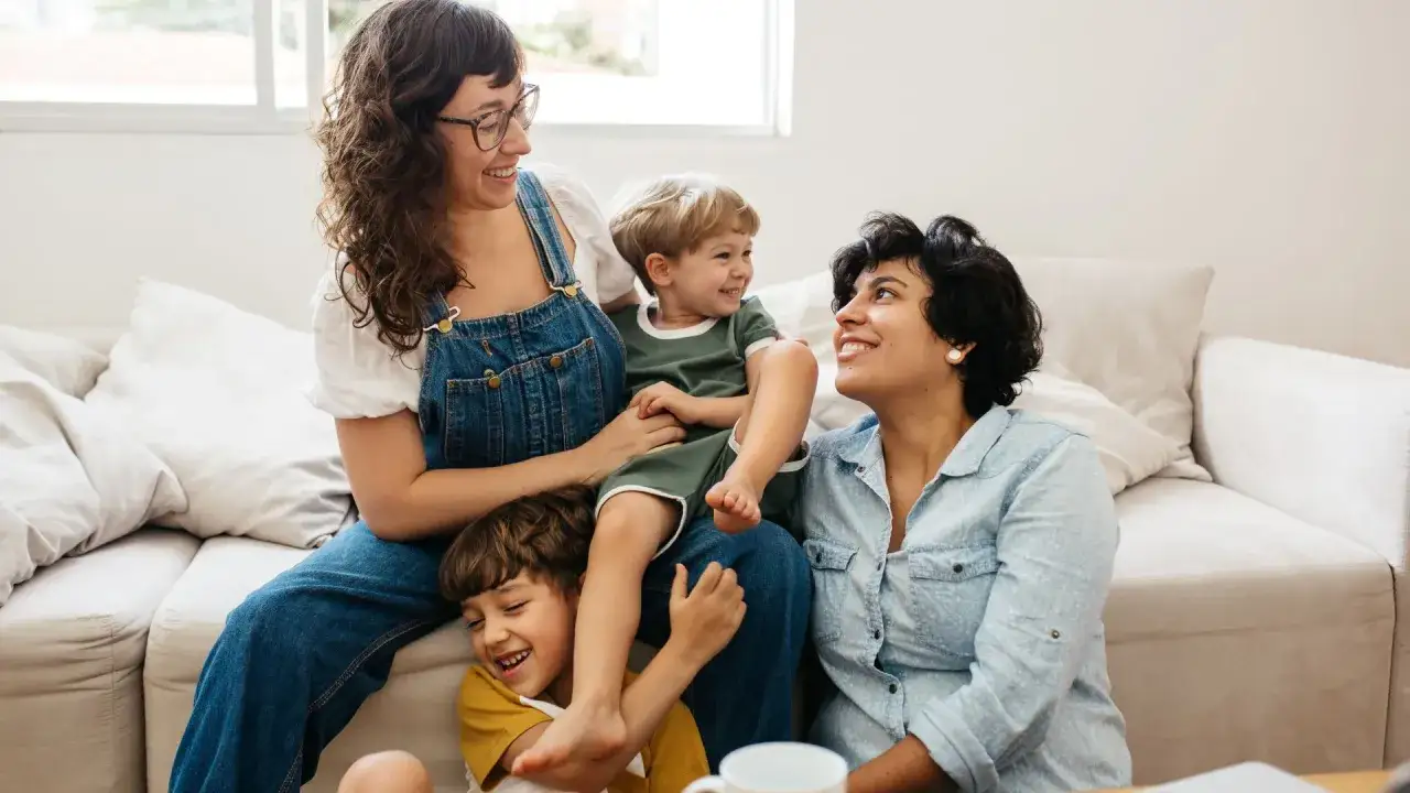Famiglia felice in soggiorno, con due mamme e i loro figli. Un momento di gioia che ricorda 3 esercizi per farsi ascoltare dai figli.