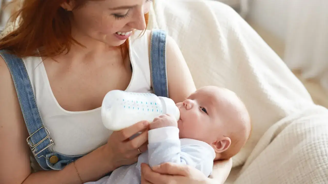 Mamma sorride mentre il suo neonato mangia ogni 2 ore latte artificiale da un biberon.