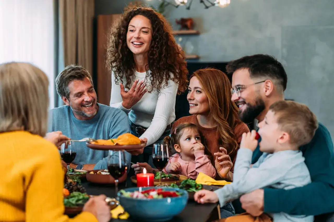 Famiglia riunita per cena: donne separate con figli e nuovi compagni condividono un momento felice e conviviale, sorridendo e mangiando insieme.