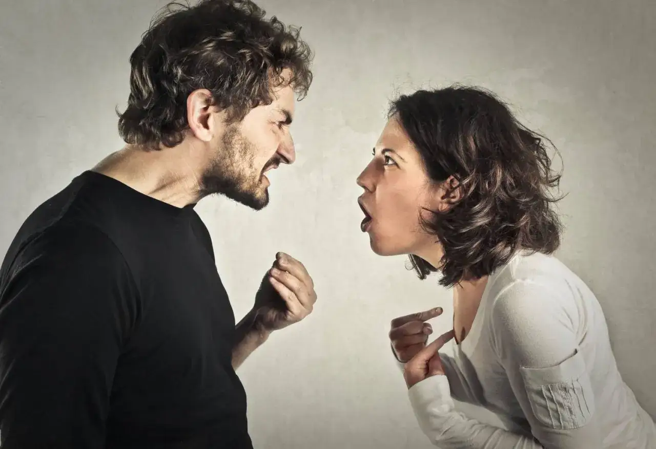 Coppia in forte discussione, con espressioni facciali intense e gesti accusatori. Un esempio di comportamento passivo aggressivo.