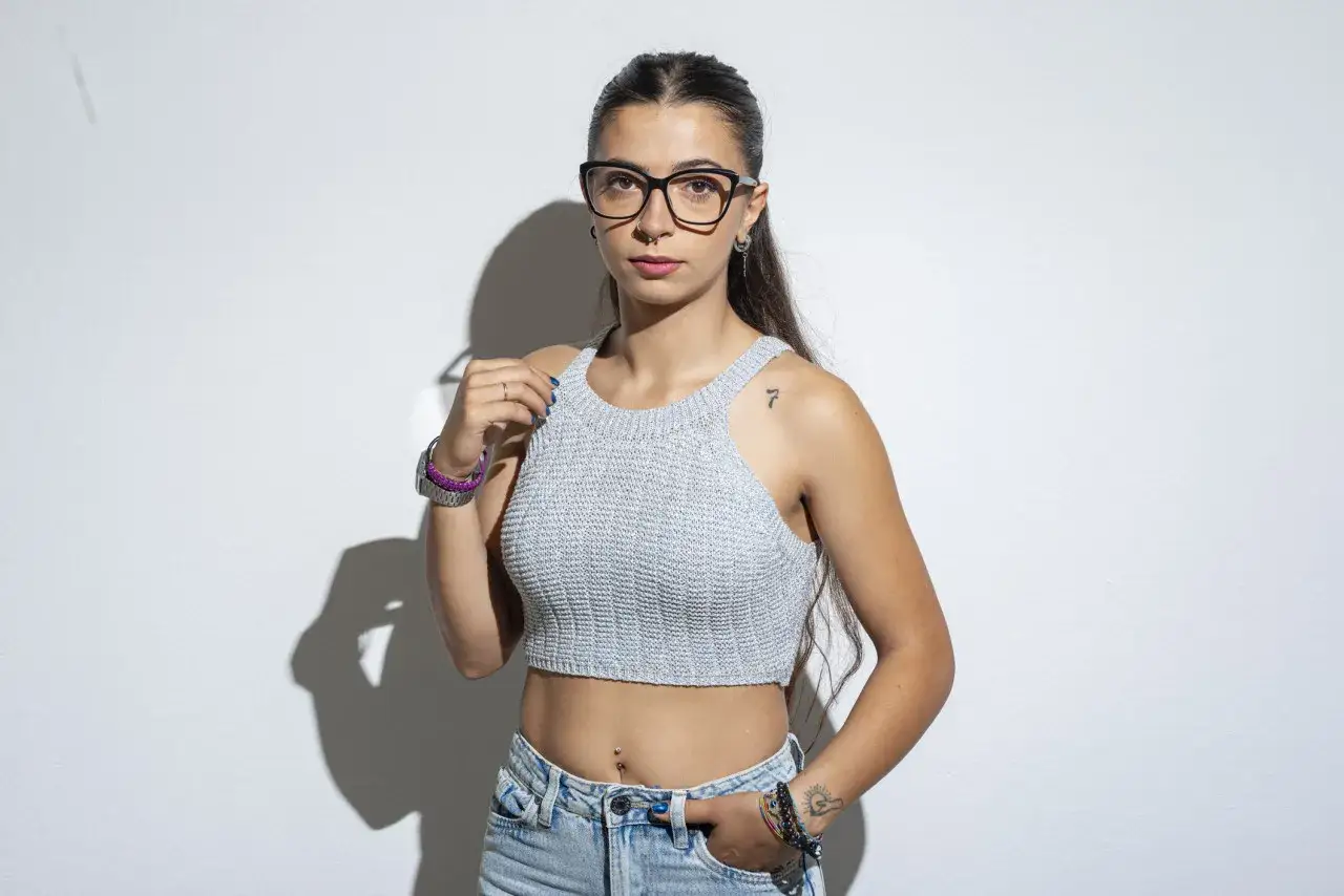 Giovane donna con occhiali e top corto, pronta a cambiare vita a 30 anni.