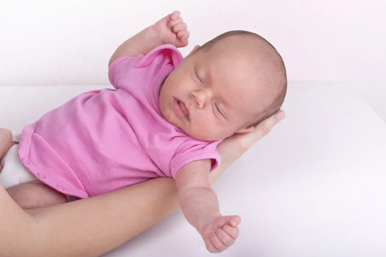 Neonato in rosa si irrigidisce e stringe i pugni, dormendo sereno tra le braccia.