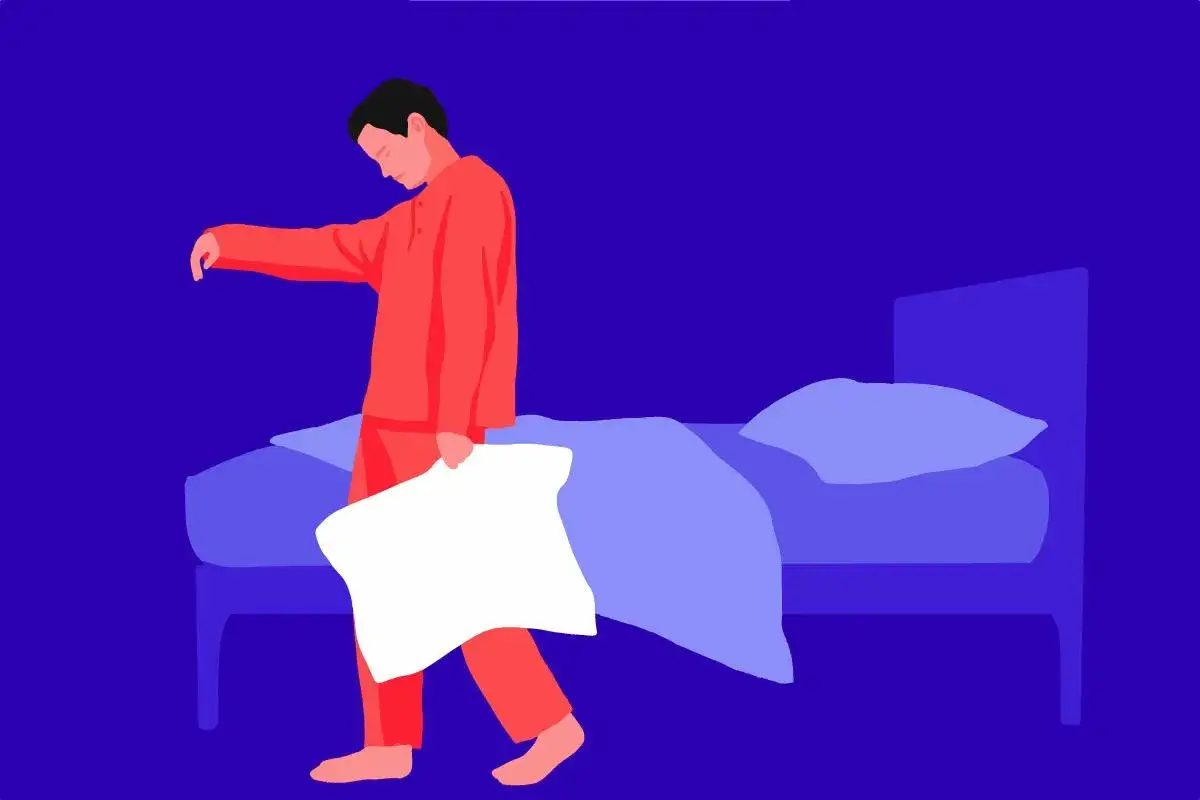 Uomo in pigiama rosso cammina nel sonno, tenendo un cuscino. Le cause psicologiche del sonnambulismo possono manifestarsi così.