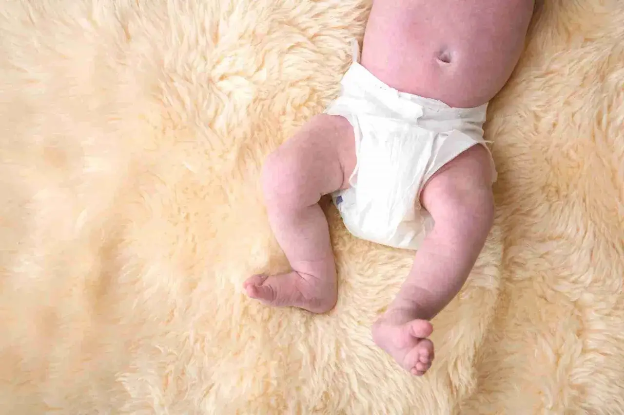 Pancia e gambe di un neonato con pannolino, sdraiato su una morbida coperta color crema. L'aria nella pancia del neonato è visibile.