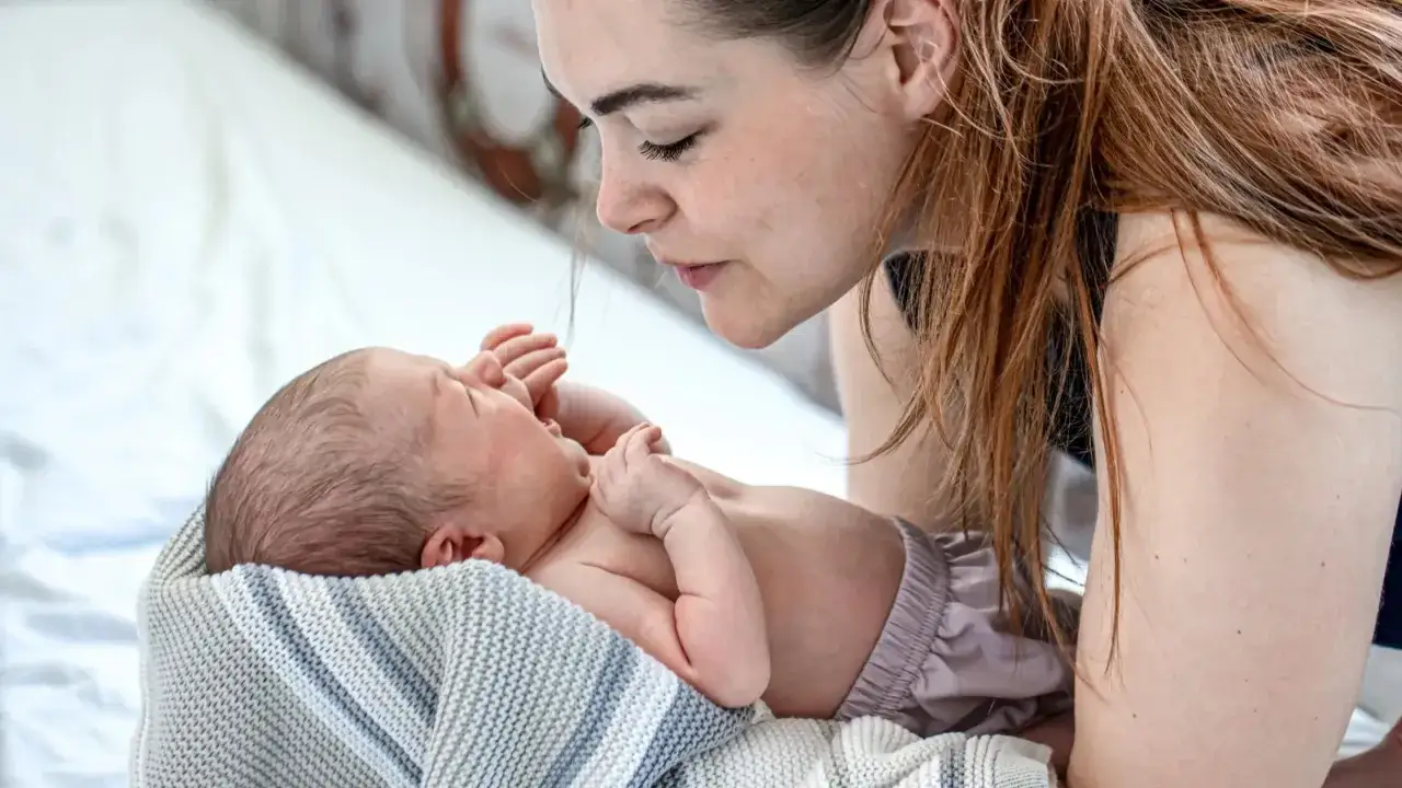 Dolce mamma guarda il suo neonato piange dopo poppata, avvolto in una coperta.