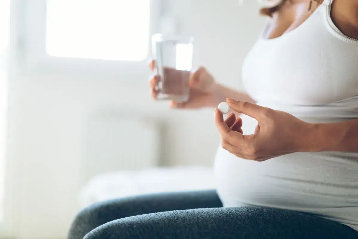 Donna incinta tiene una pillola e un bicchiere d'acqua. L'uso di cortisone in gravidanza richiede cautela.
