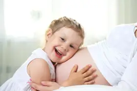 Bambina di 3 anni felice abbraccia la pancia della mamma, in attesa dell'arrivo di un fratellino.