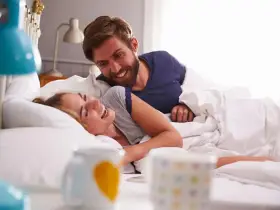Coppia sorridente a letto, un momento di gioia che va oltre i rapporti promiscui, un legame profondo.