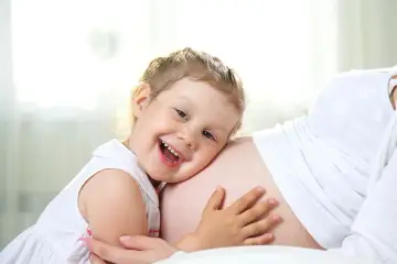 Bambina di 3 anni felice abbraccia la pancia della mamma, in attesa dell'arrivo di un fratellino.