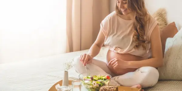 Donna incinta sorride mangiando un'insalata fresca. Il burro in gravidanza è un alimento importante per la crescita del feto.
