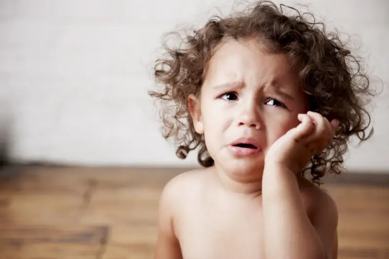 Bambino con riccioli castani piange, forse è un modo per comunicare il disagio, ecco perchè i bambini mordono.