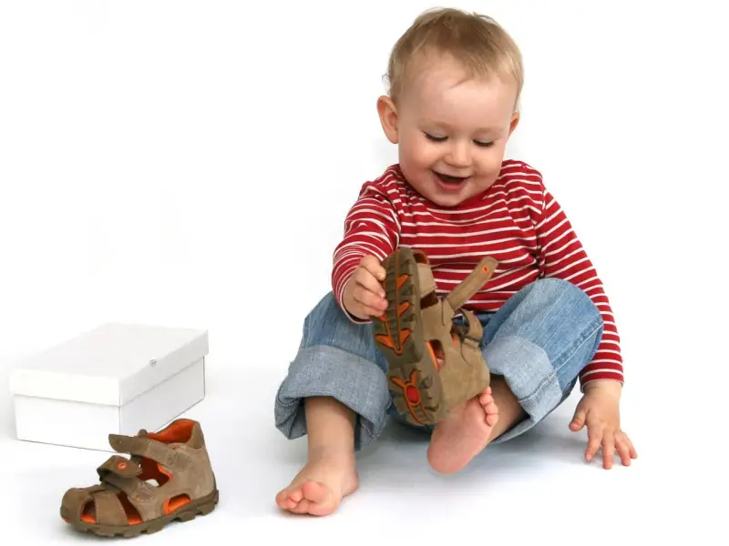 Bambino di 18 mesi, con un comportamento curioso, gioca con un sandalo marrone.