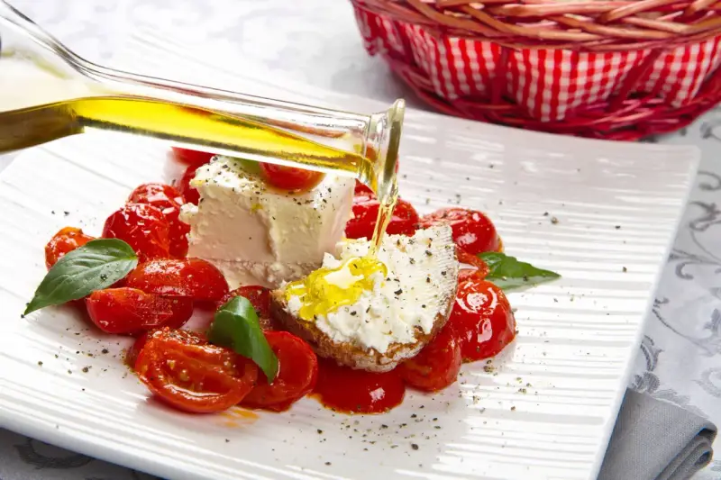 Un piatto di pomodorini confit con robiola, perfetto per una gravidanza sana e gustosa. Olio d'oliva versato su una fetta di pane con formaggio.